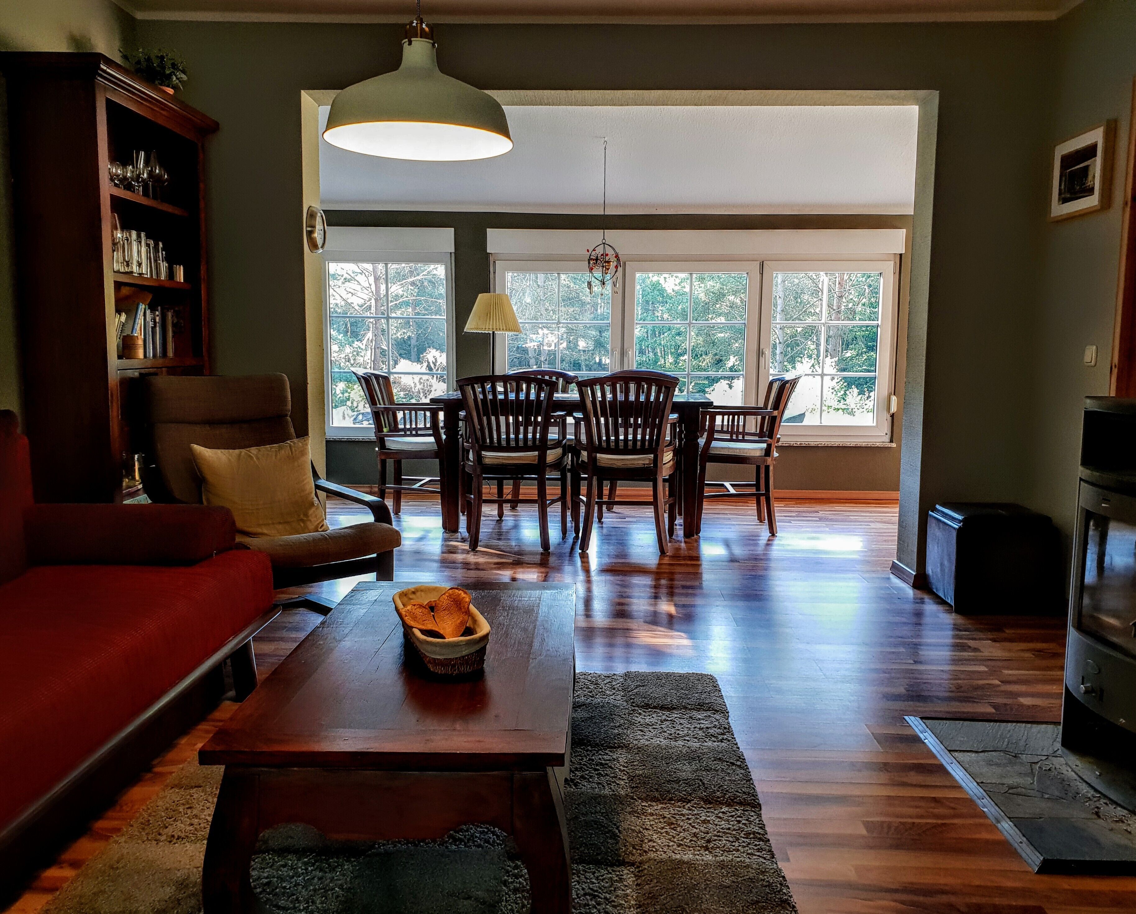 Uma sala de estar ampla, com um sofá vermelho, uma mesa de centro de madeira e uma área de jantar com cadeiras e mesa de madeira.