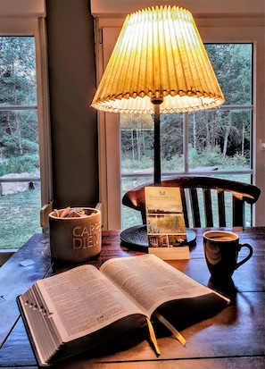 A wooden table with a book, a coffee cup, a candle holder, and a lamp.