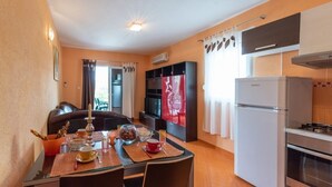 A compact kitchen with a refrigerator, oven, and a dining area with a table set for two. - Apartment in Vinišće with Balcony, Air condition, WIFI, Washing machine (4753-1) (Vinišce)