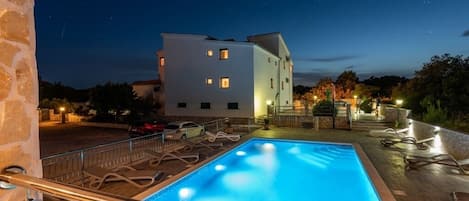 Ein Schwimmbecken mit Holzterrasse und Metallgeländern, umgeben von einer Steinmauer.