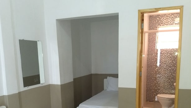 A hotel room with a bed, a small bedside table, a mirror, and a bathroom visible through an open door. - Hotel Aruba (Curitiba)