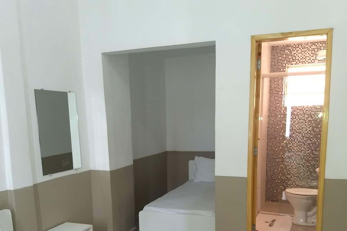 Ein Hotelzimmer mit einem Bett, einem kleinen Nachttisch, einem Spiegel und einem durch eine offene Tür einsehbaren Badezimmer.