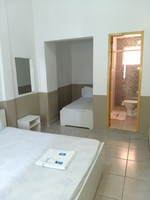 A hotel room with a bed, a small bedside table, a mirror, and a bathroom visible through an open door. - Hotel Aruba (Curitiba)