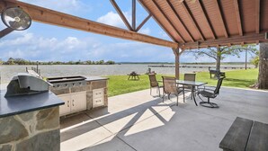 An outdoor patio with a stone grill, seating, and a view of the lake. - Life is Better at the Lake. Come relax at FishCamp@PK (Graford)