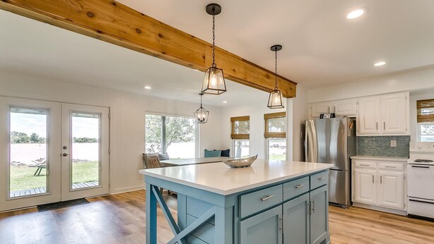 A spacious kitchen with a large island, wooden ceiling beams, and a view to the outdoors. - Life is Better at the Lake. Come relax at FishCamp@PK (Graford)