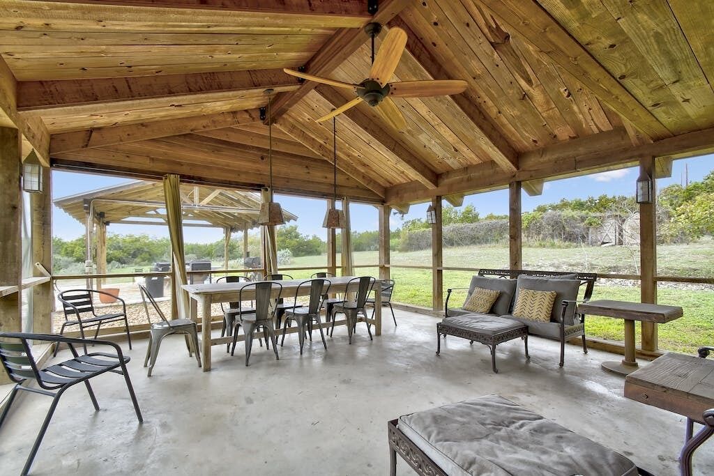 A covered outdoor seating area with wooden beams, a ceiling fan, and a view of the outdoors.