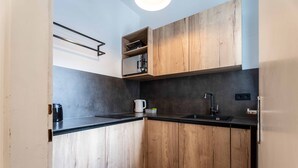 A compact kitchen with wooden cabinets, a black countertop, a coffee maker, and a kettle. - Living Eden - TOP 3, city center & balcony (Zell am See)