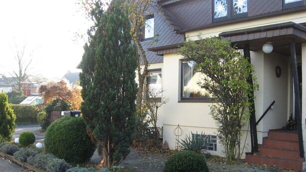 A two-story house with a well-maintained garden, a visible staircase, and a clear sky. - Many excursion destinations, e.g. Museumsdorf, wildlife park, Altes Land, opera, theater and musical. (Hamburg)