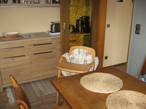 A compact kitchen with wooden cabinets, a dining table with two woven placemats, a chair with a patterned cushion, and a toaster on the counter. - Many excursion destinations, e.g. Museumsdorf, wildlife park, Altes Land, opera, theater and musical. (Hamburg)