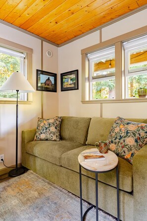A cozy room with a green sofa, a small table with a book, and two framed pictures on the wall.