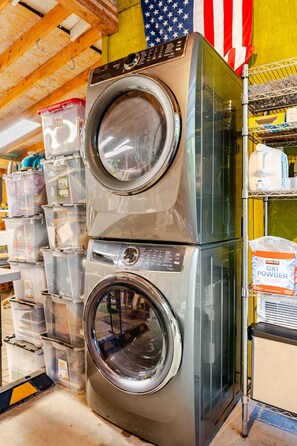 A stacked washer and dryer in a store with storage bins and cleaning supplies in the background.