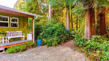A cabin with a porch, a bench, and a gravel path leading into a forest.