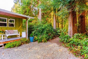 A cabin with a porch, a bench, and a gravel path leading into a forest.
