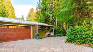 A two-story building with a garage, a covered porch, and a gravel driveway. - Wooded Bainbridge Island Studio (Bainbridge Island)