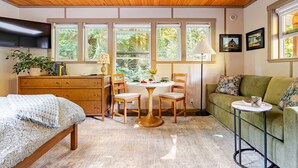 A cozy room with a wooden ceiling, a bed, a green sofa, a dining table with chairs, and a TV mounted on the wall. - Wooded Bainbridge Island Studio (Bainbridge Island)