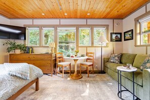 Un'accogliente stanza con soffitto in legno, un letto, un divano verde, un tavolo da pranzo con sedie e un televisore montato a parete.