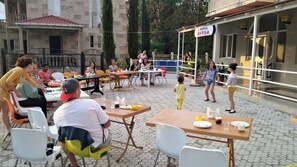 An outdoor dining area with tables and chairs, a sign for 'HOTEL RITSA', and a building in the background. - Hotel Ritsa (Ureki)