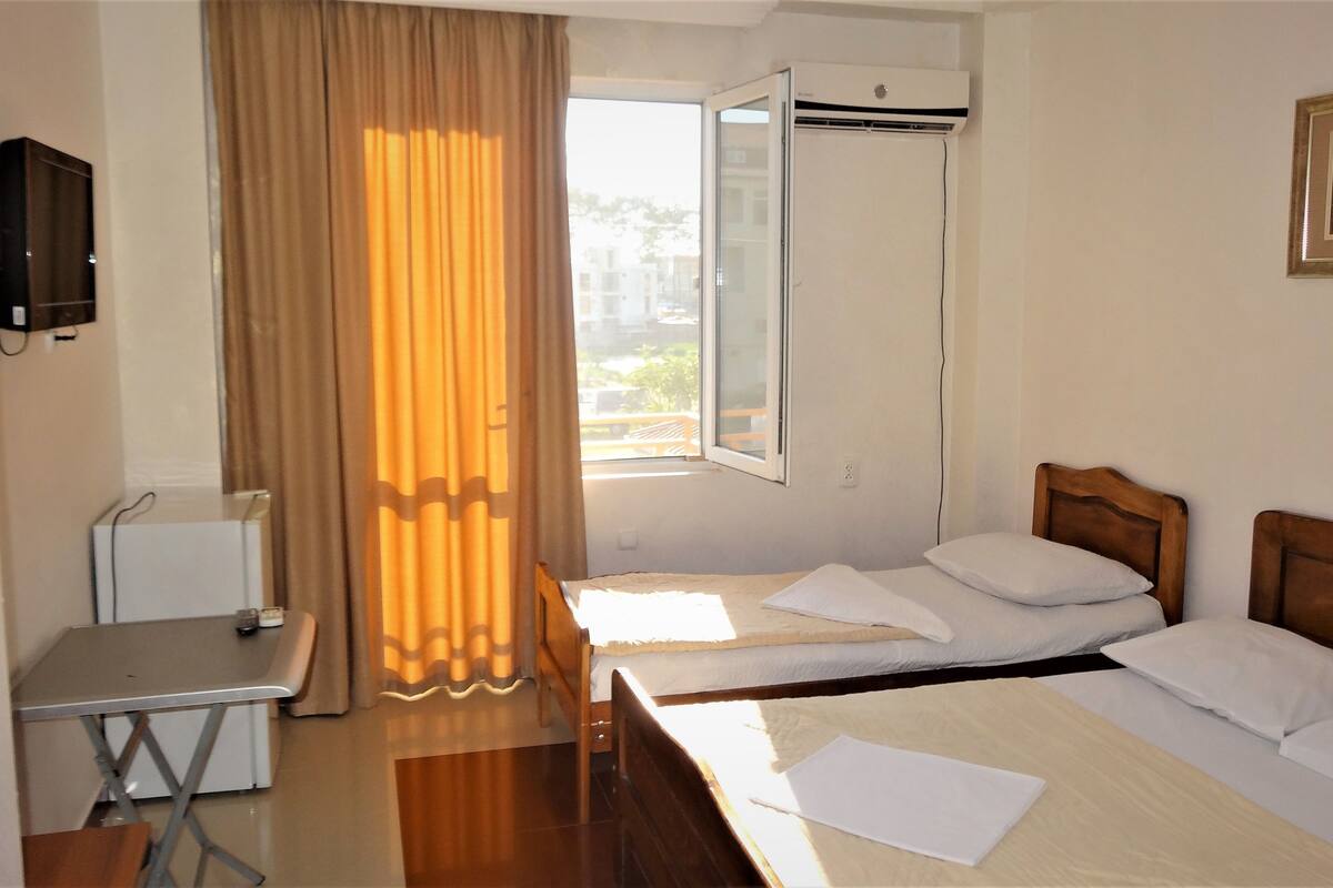 A hotel room with two beds, a desk, a chair, an air conditioning unit, and a window with curtains.