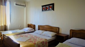 A hotel room with two single beds, each with a wooden headboard, white bedding, and a floral-patterned bedspread. There is a small bedside table with a lamp on one side and a wall-mounted air conditioning unit above the beds. A framed picture of red flowers hangs on the wall. - Hotel Ritsa (Ureki)