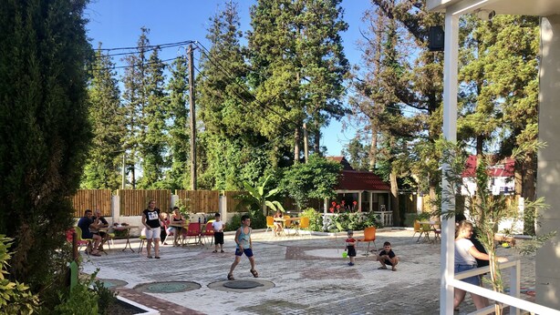 Un patio al aire libre con suelo de baldosas, rodeado de árboles y un edificio con techo rojo.