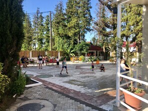 An outdoor patio area with tiled flooring, surrounded by trees and a building with a red roof. - Hotel Ritsa (Ureki)