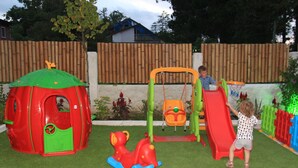 Un área de juegos infantiles con un tobogán, columpios y una casita.