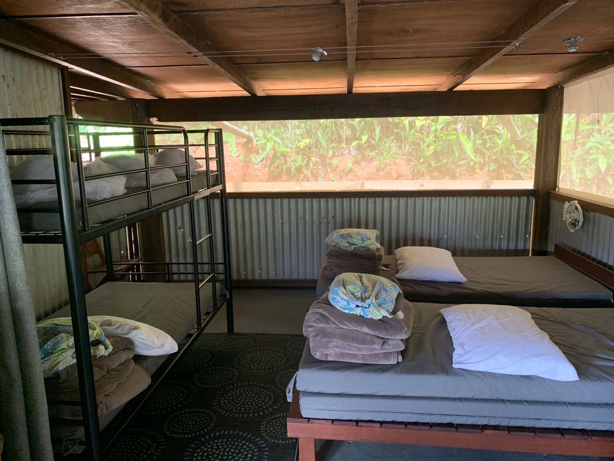 A dormitory room with bunk beds, a single bed, and a window with a view of greenery.