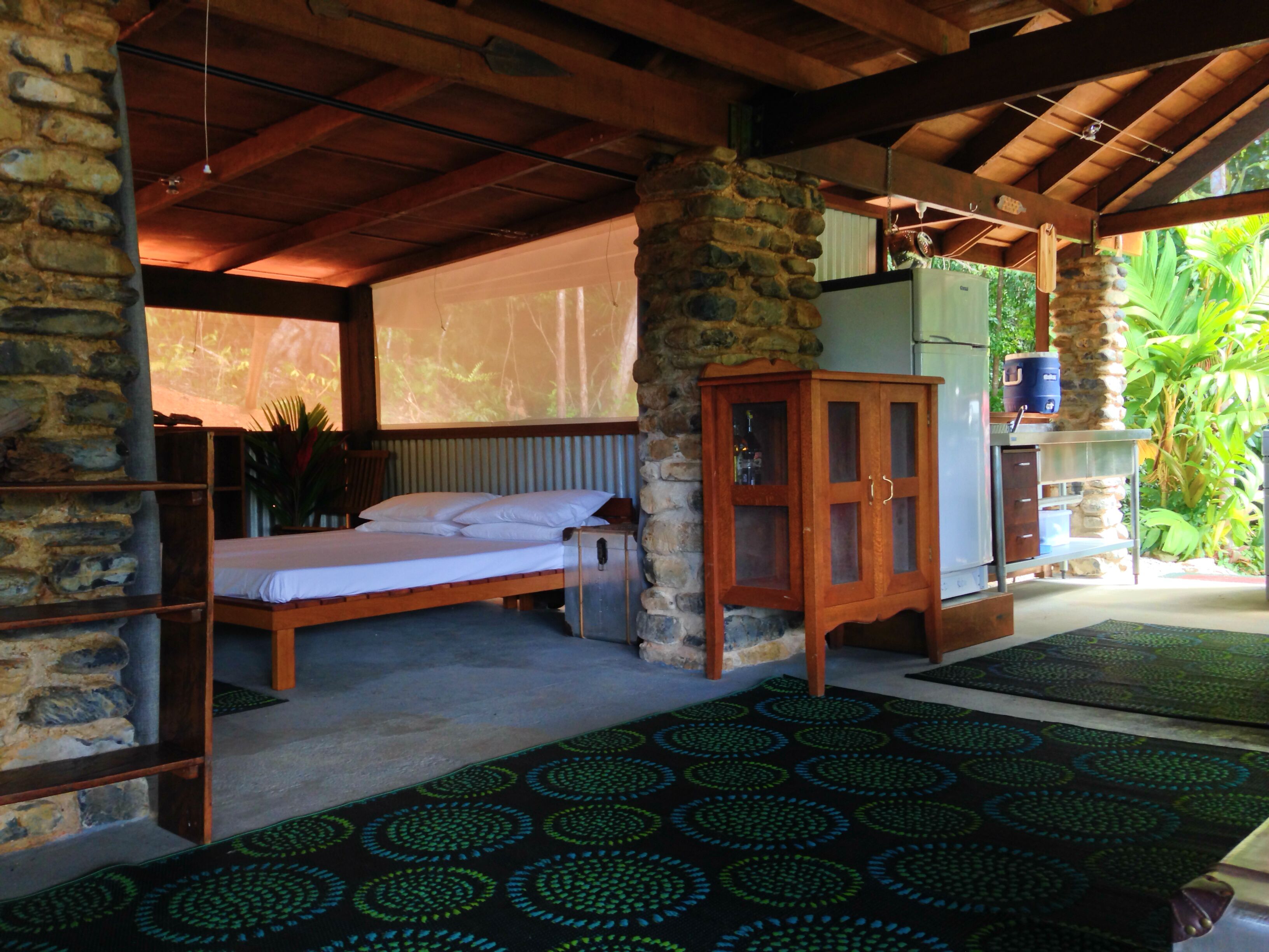 A room with a bed, a wooden cabinet, and a stone wall.