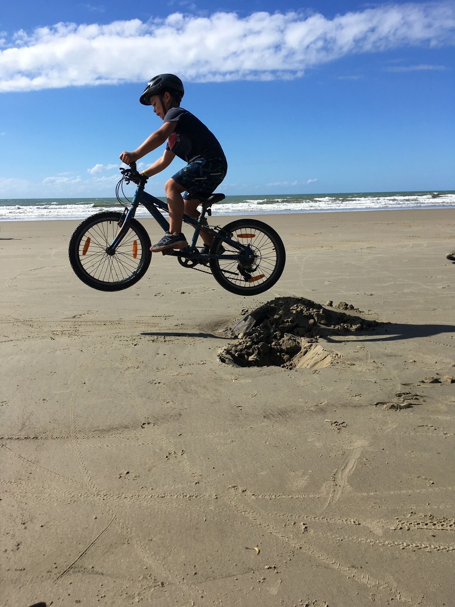A person riding a bicycle on a sandy beach with ocean waves in the background.