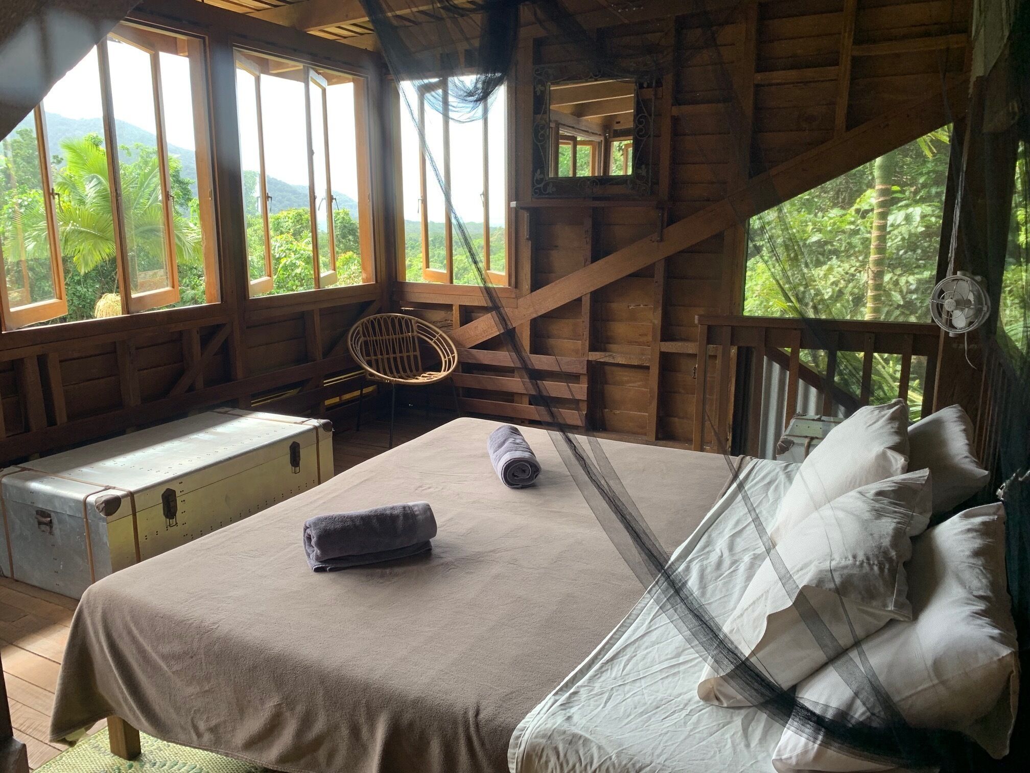 A wooden cabin room with a bed, a bench, and a view of the forest.