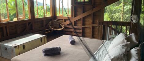 A wooden cabin room with a bed, a bench, and a view of the forest.