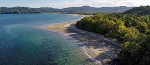 Un paisaje costero con playa, aguas cristalinas y colinas boscosas circundantes.