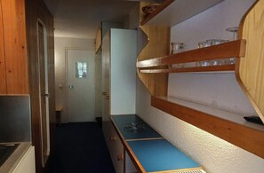 Una cocina estrecha con armarios de madera, una encimera azul y un estante empotrado con frascos.