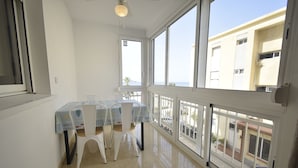 Un balcón con mesa y sillas, ventanas amplias y vistas a edificios.