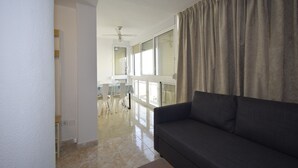 Una sala de estar con un sofá gris, un ventilador de techo y un comedor con sillas y una mesa.