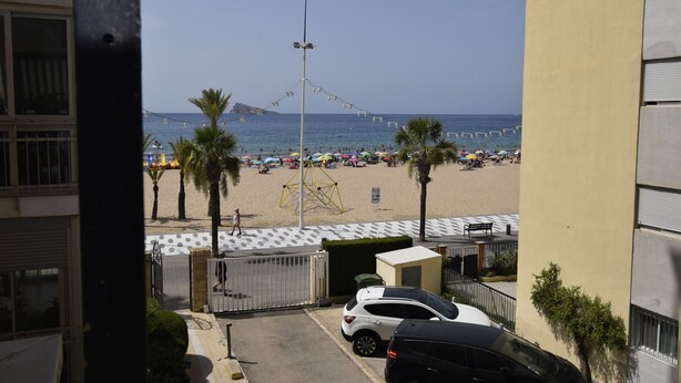 Vista de una playa con palmeras, un coche blanco y un edificio con entrada protegida.