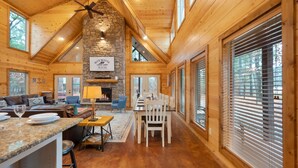 Un intérieur spacieux de chalet en bois, avec une cheminée en pierre, un plafond en bois et de grandes fenêtres.