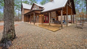 Une cabane en rondins dotée d’un porche couvert, d’une cheminée en pierre et d’une allée en gravier.