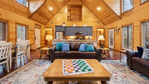 L’intérieur chaleureux d’un chalet en bois comprend un coin repas, un salon avec un jeu d’échecs et une cuisine équipée d’appareils électroménagers modernes.