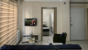A modern living room with a flat-screen TV, a sofa, a coffee table, and a bedroom visible through an open door. - Edirne Apart (Edirne)