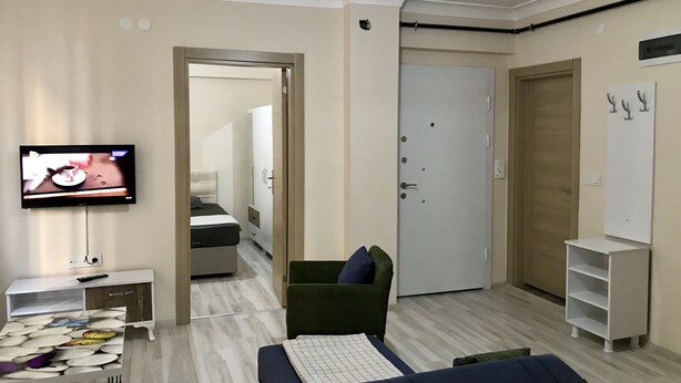 A modern living room with a sofa, a television, and a small table. There is a door leading to another room and a cabinet with a shelf. - Edirne Apart (Edirne)