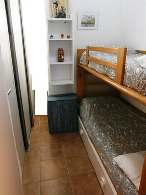 Quarto pequeno e compacto com uma cama beliche, uma estante com objetos decorativos e um pequeno armário.