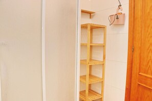 Un estante de madera en un baño con pared de azulejos blancos y puerta de madera.