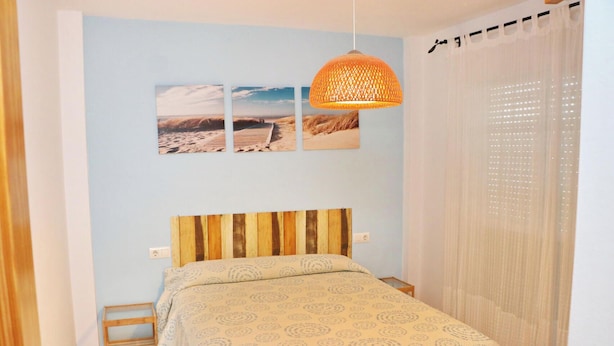 Ein Schlafzimmer mit einem hölzernen Kopfteil, einem Bett mit gemusterten Betttextilien, einem kleinen Nachttisch und einer Wandlampe.