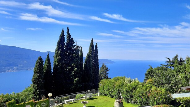 A scenic view of a coastal area with tall cypress trees, a bench, and a pathway leading to a scenic overlook. - Appartamento 105 Benaco (Tignale)