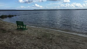En strand med en grøn bænk, roligt vand og en fjerntliggende kystlinje.