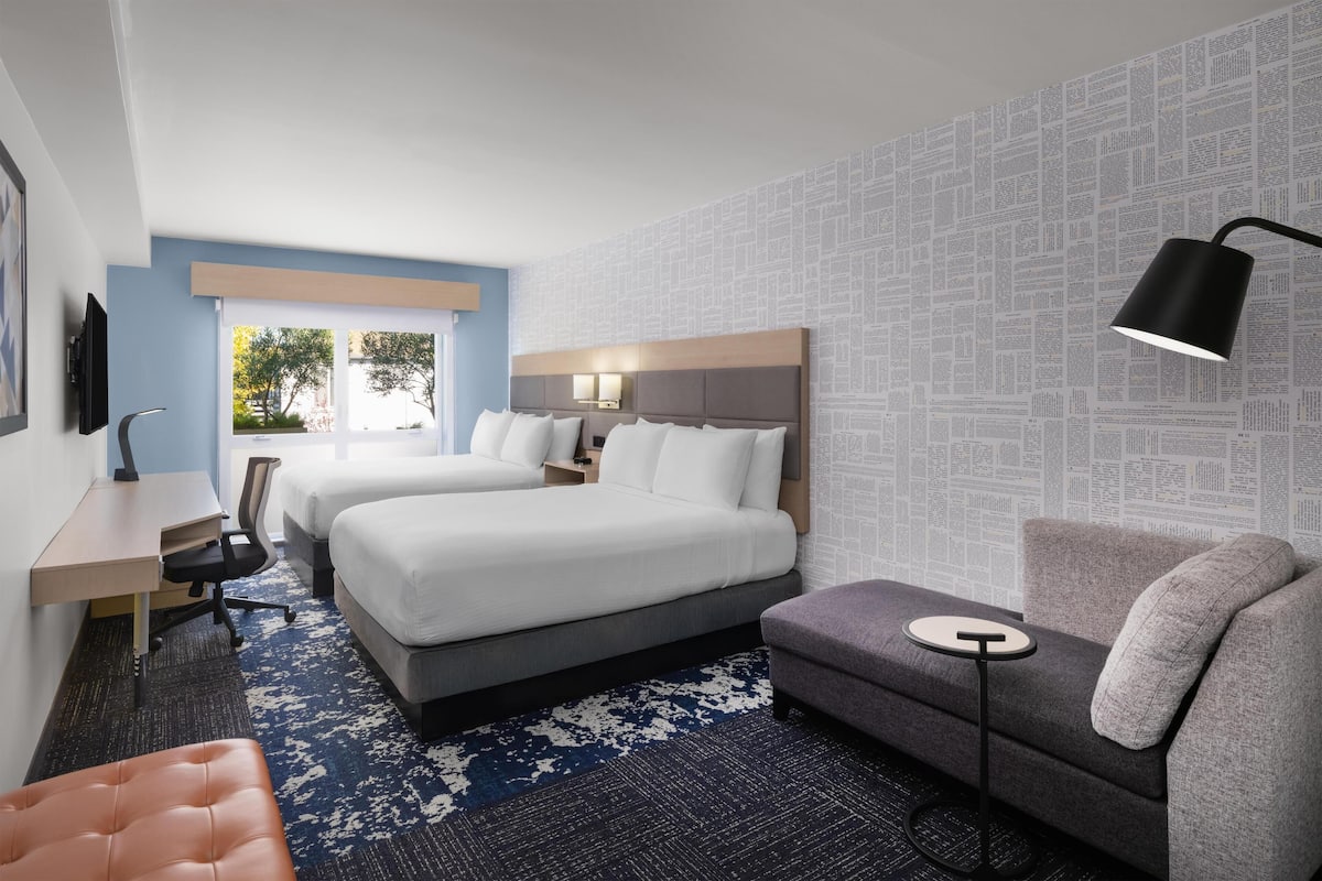 A hotel room with two beds, a desk, a sofa, and a TV.