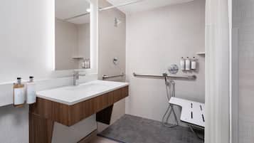 A modern bathroom with a large mirror, a wooden vanity, a shower with a handheld showerhead, and a grab bar.