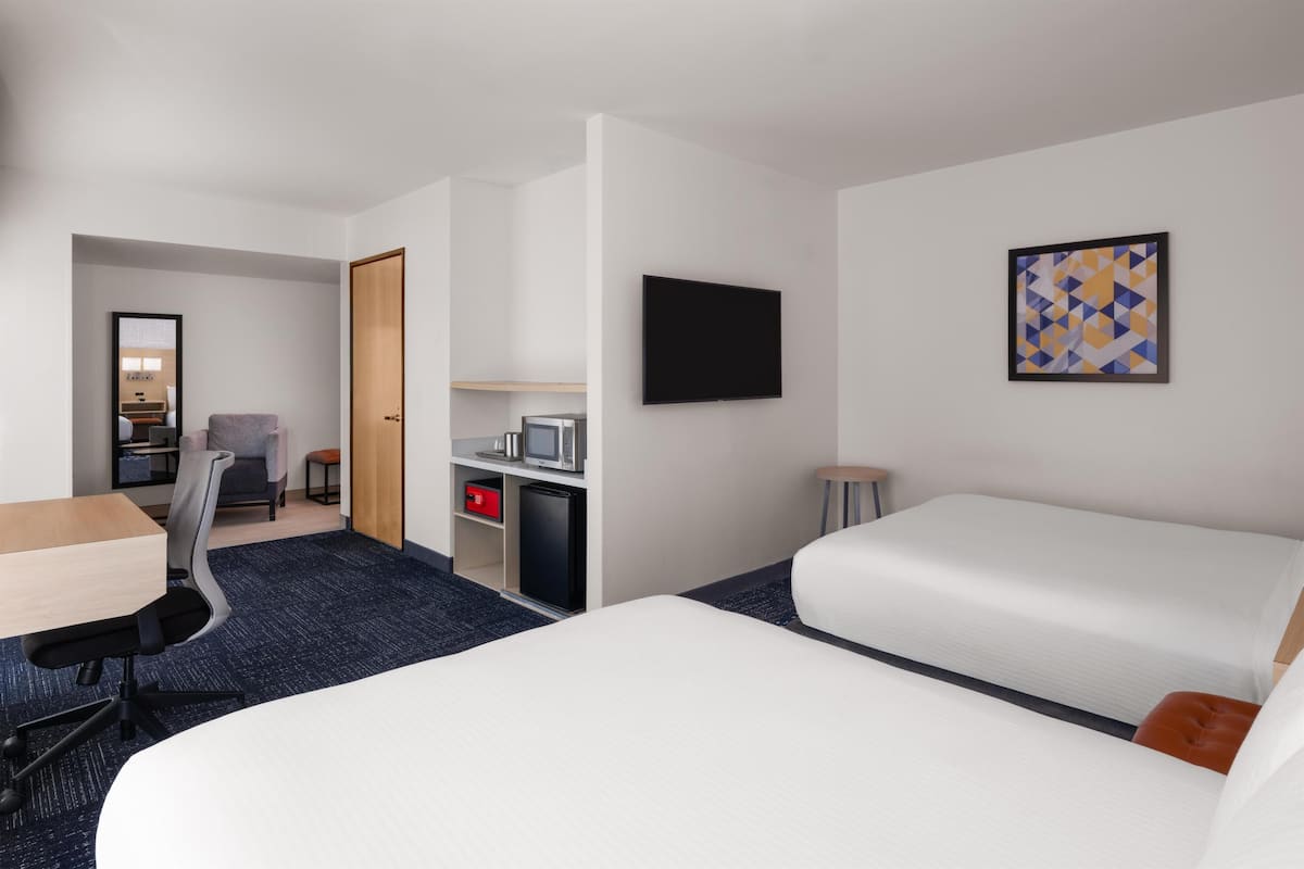 A hotel room with a bed, a desk, a chair, a TV, and a small kitchenette.