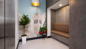 Un moderno vestíbulo con área de descanso, un mural de un edificio y plantas en macetas.